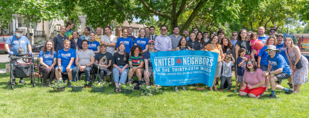 UN35 members arranged in two rows, with potted plants in the foreground and a large tree in the background.